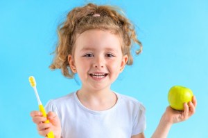 Child holding apple and toothbrush